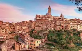 Italy Moto Tours Panoramic view of Siena at sunset with its famous cathedral rising above medieval rooftops in Tuscany, Italy.