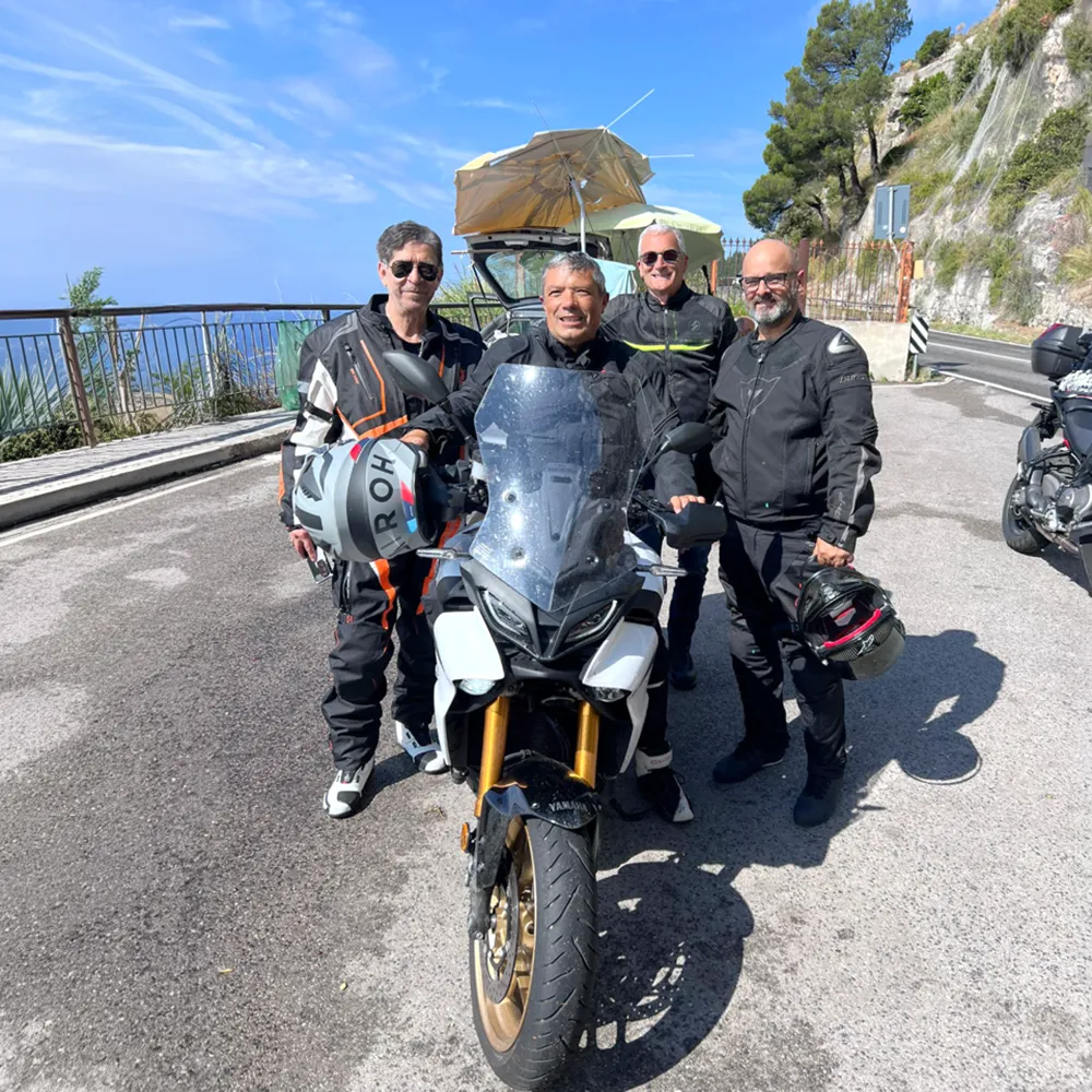 Italy Moto Tours Four bikers posing with a Yamaha motorcycle on the Amalfi Coast during a sunny group ride organized by Italy Moto Tours
