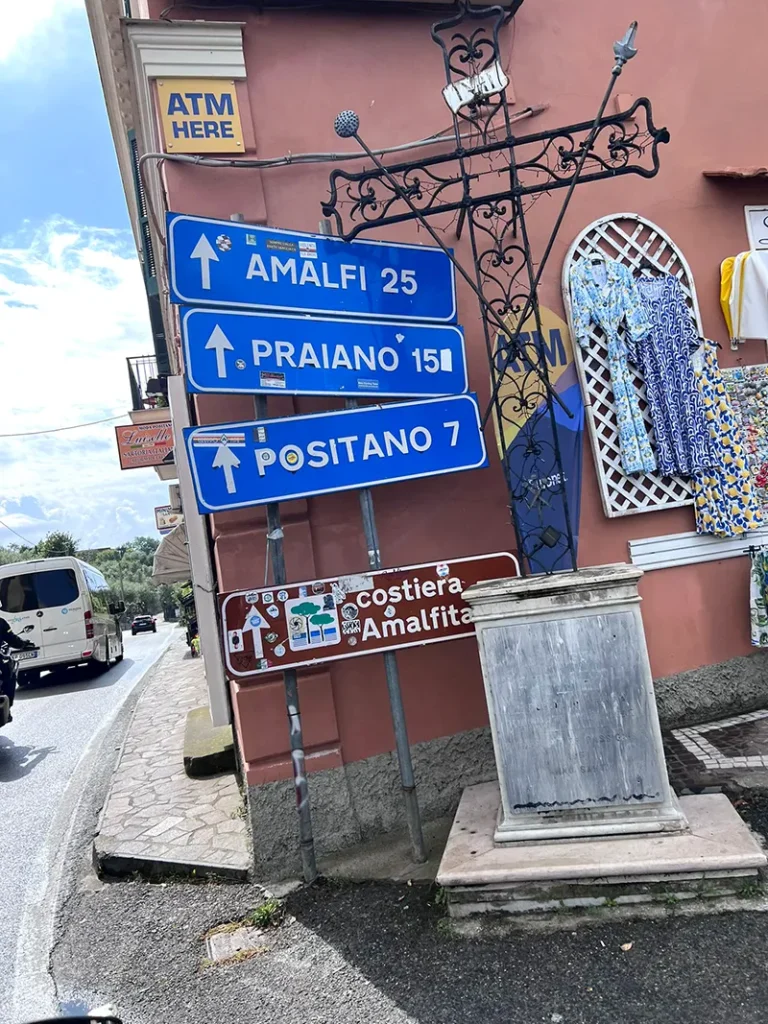 Italy Moto Tours Blue road signs pointing to Amalfi, Praiano, and Positano along the Amalfi Coast, captured during an Italy Moto Tours scenic ride