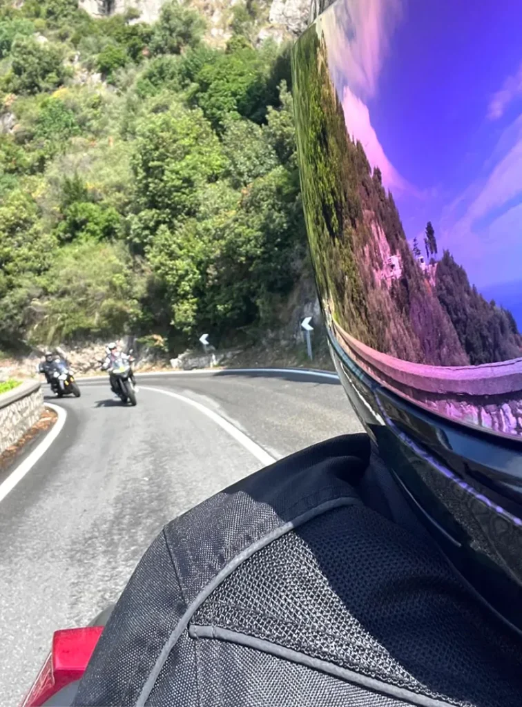 Italy Moto Tours Motorcyclist’s helmet reflecting coastal cliffs and road as riders cruise along a scenic curve on the Amalfi Coast with Italy Moto Tours