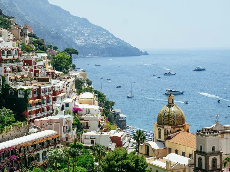 Colorful hillside buildings and the Church of Santa Maria Assunta dome in Positano overlooking the sea during a motorbike tour