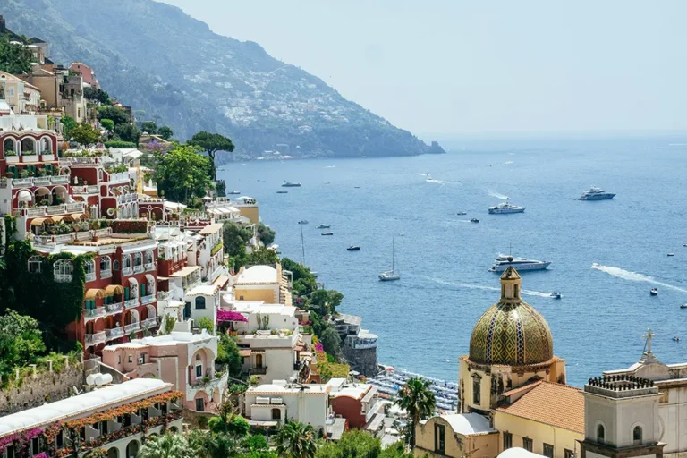 Colorful hillside buildings and the Church of Santa Maria Assunta dome in Positano overlooking the sea during a motorbike tour