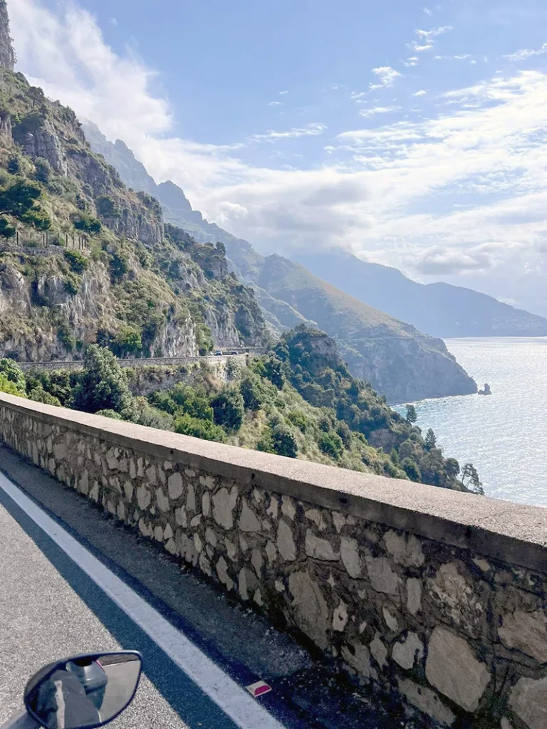 Italy Moto Tours View of the winding Amalfi Coast road carved into cliffs above the sea, captured during a motorcycle tour with Italy Moto Tours