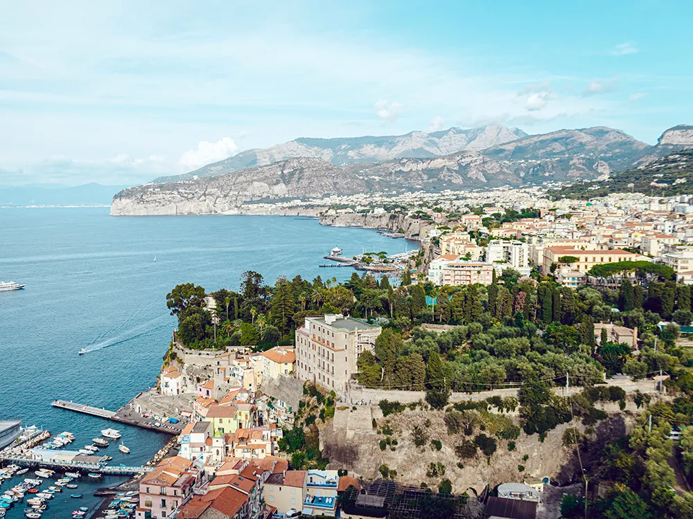 Italy Moto Tours Panoramic view of Sorrento Coast with colorful buildings, marina, and dramatic cliffs during a motorbike tour in Italy
