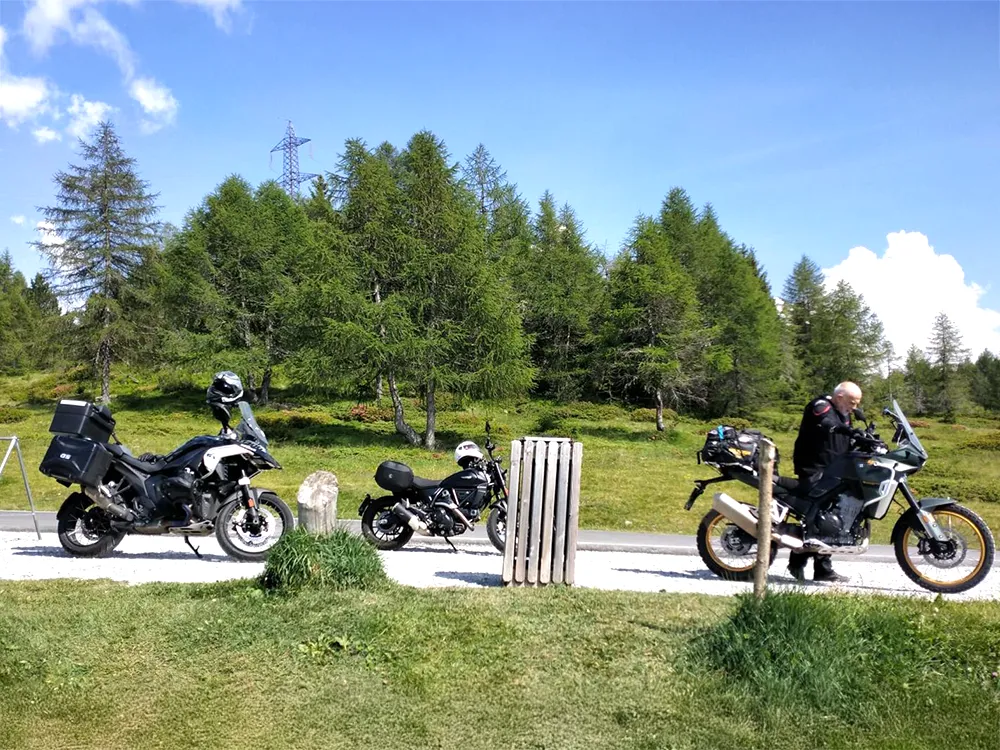 Guided pit stop in the Dolomites: Italy MotoTours bikes parked beside alpine meadow while rider adjusts gear