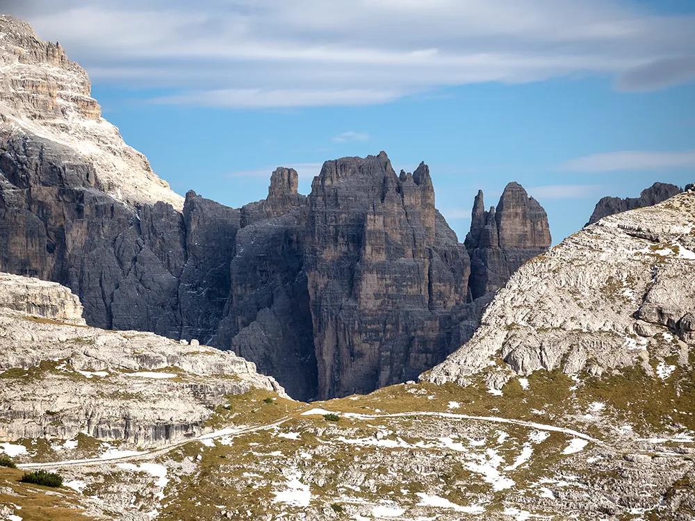 Dramatic rock spires of the Sella Group with winding high-mountain road and lingering spring snow