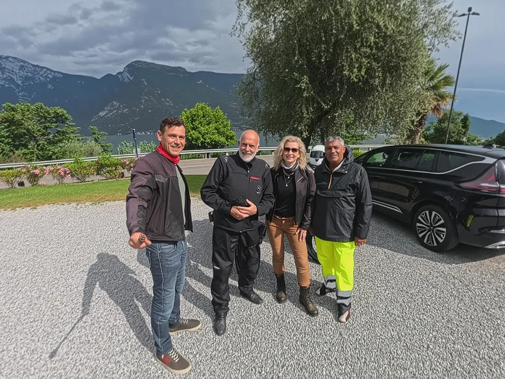 Selfie: rider, guide Mario Menicocci, happy couple, and owner Alessio pose on Dolomites tour with lake and peaks behind