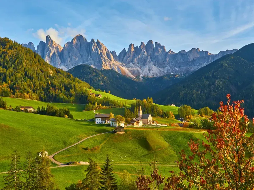 Italy Moto Tours A picturesque village in the Dolomites surrounded by green hills and jagged mountain peaks under a clear blue sky