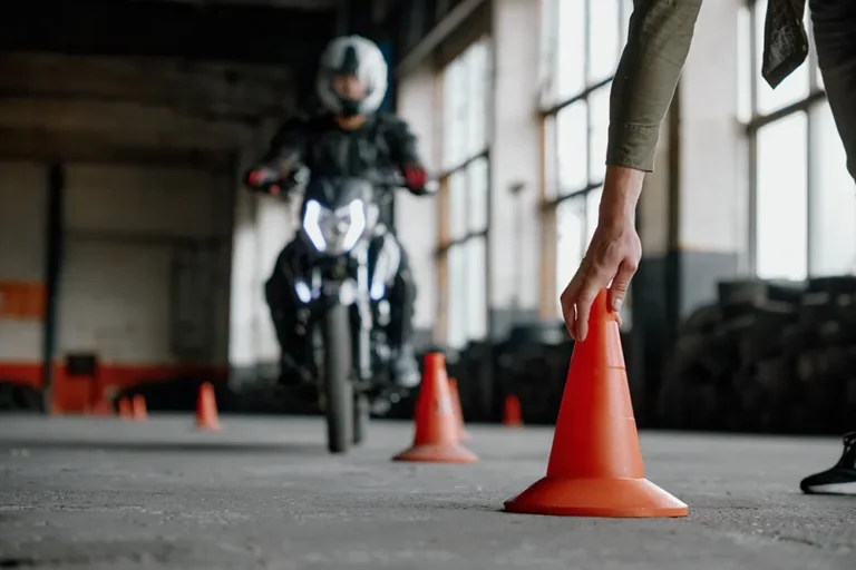 Italy Moto Tours Rider in full gear navigates orange safety cones during an indoor slow-speed training session while instructor sets the course markers.