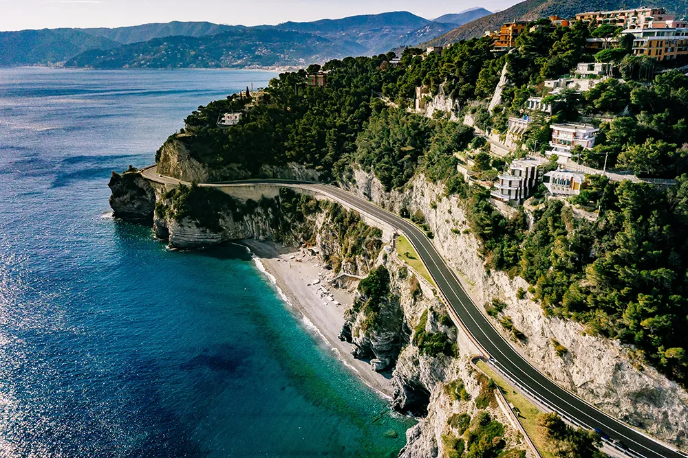 Italy Moto Tours Drone view of winding cliffside road on the Italian Riviera above turquoise sea—stretch featured in Italy Moto Tours routes.