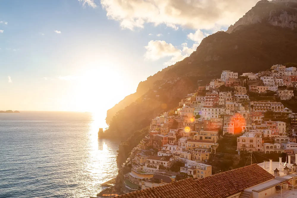 Italy Moto Tours Golden sunset bathes Positano’s pastel terraced houses perched on steep Amalfi Coast cliffs above the shimmering Tyrrhenian Sea.