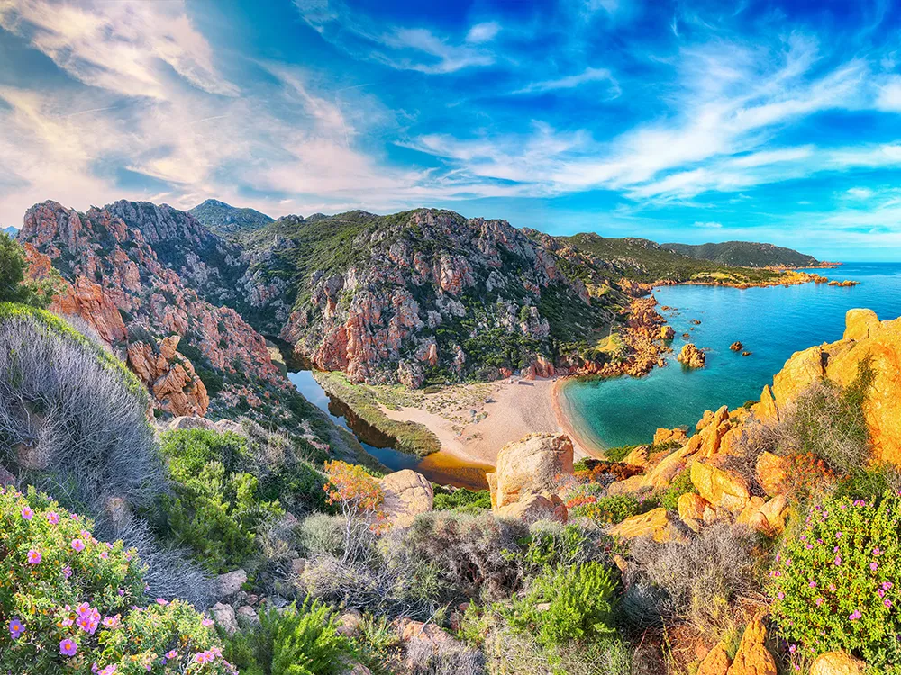 Italy Moto Tours Breathtaking view of Li Cossi Beach with turquoise waters, rugged cliffs, and wild Mediterranean flora