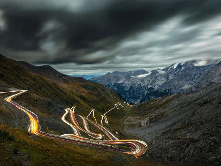 Night light trails on Stelvio Pass hairpins under a stormy alpine sky