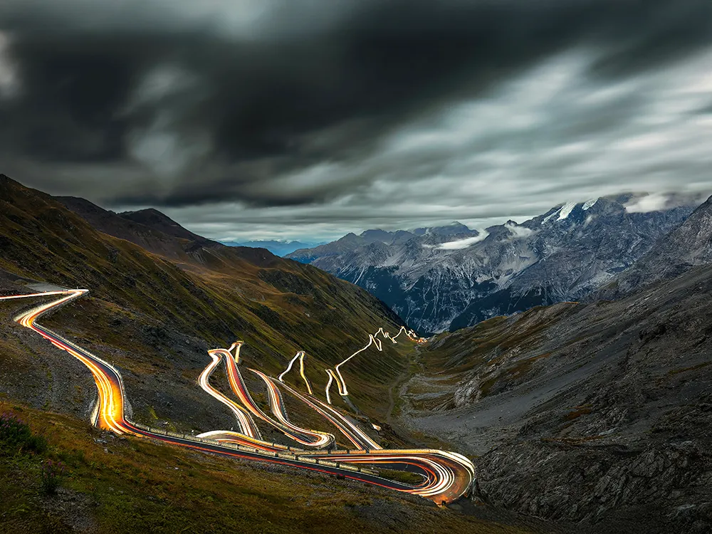 Night light trails on Stelvio Pass hairpins under a stormy alpine sky