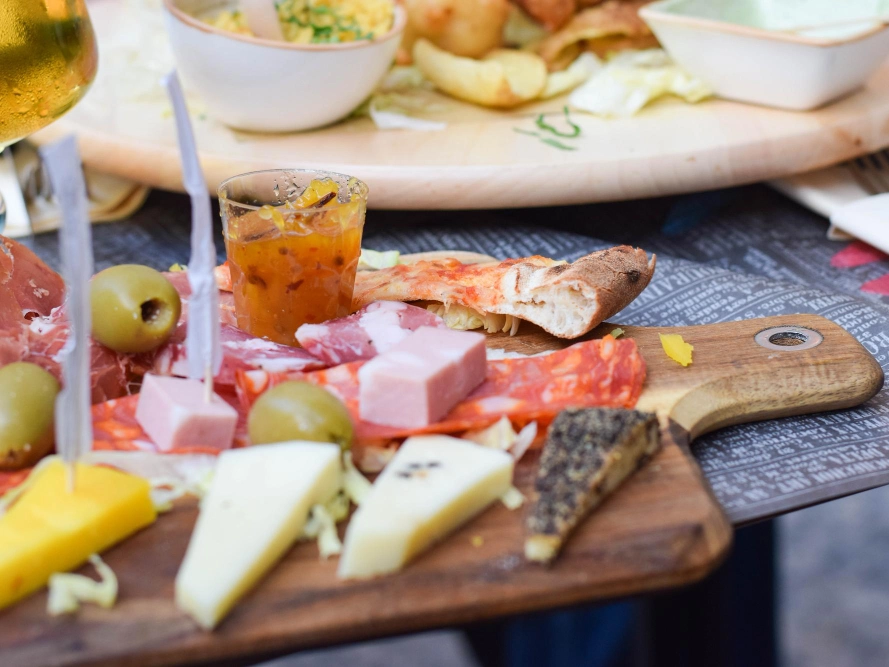 Italy Moto Tours Close-up of an Italian charcuterie board with cured meats, assorted cheeses, olives, and bread on a wooden plank