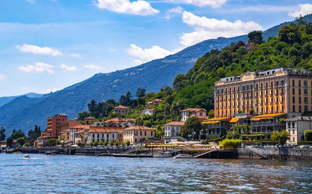 Italy Moto Tours Lakeside view of Grand Hotel Tremezzo with colorful façades against lush green hills under blue sky