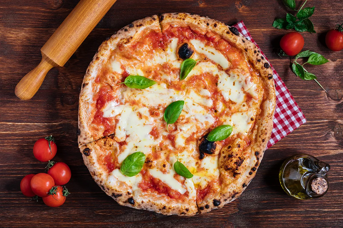 Close-up of a wood-fired Neapolitan Margherita pizza with fresh basil leaves on a rustic wooden table