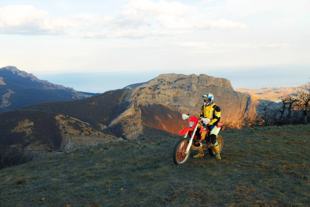 Italy Moto Tours The enduro motorcycle is parked on a rocky summit, where the sunset bathes the surrounding mountains in golden light.