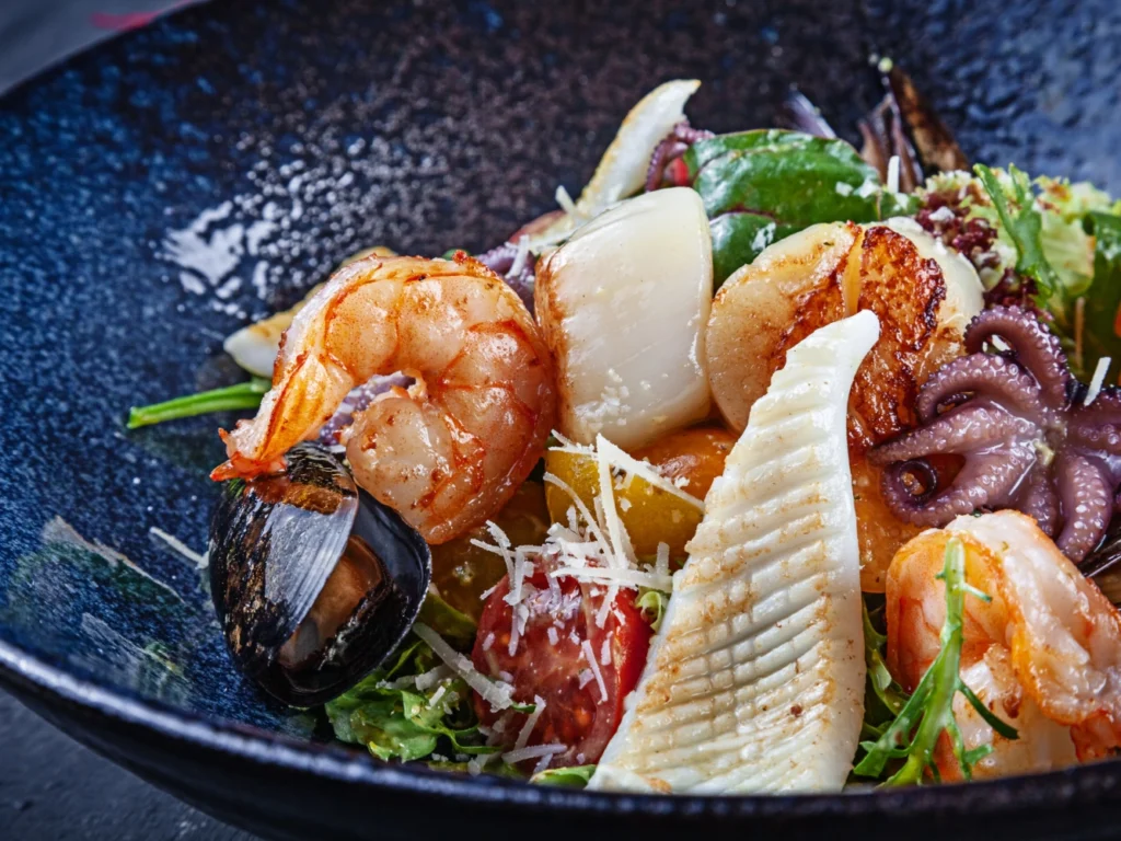 Italy Moto Tours Close-up of Italian seafood salad with shrimp, scallops, squid, octopus and mussels over greens with cherry tomatoes and Parmesan.