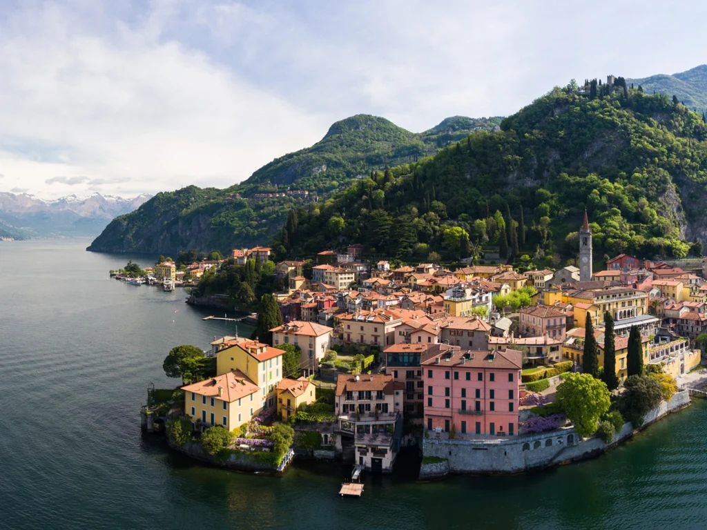 Italy Moto Tours Aerial view of Varenna on Lake Como—pastel houses, bell tower, and Alpine backdrop over deep-blue water.