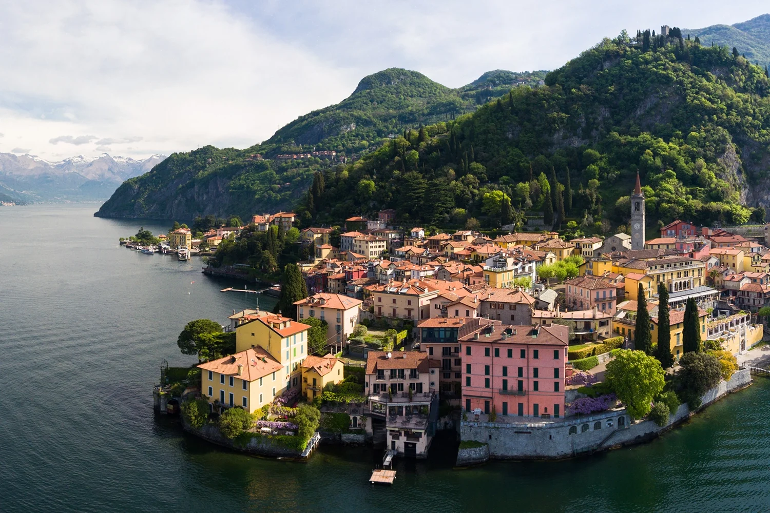 Aerial view of Varenna on Lake Como—pastel houses, bell tower, and Alpine backdrop over deep-blue water.