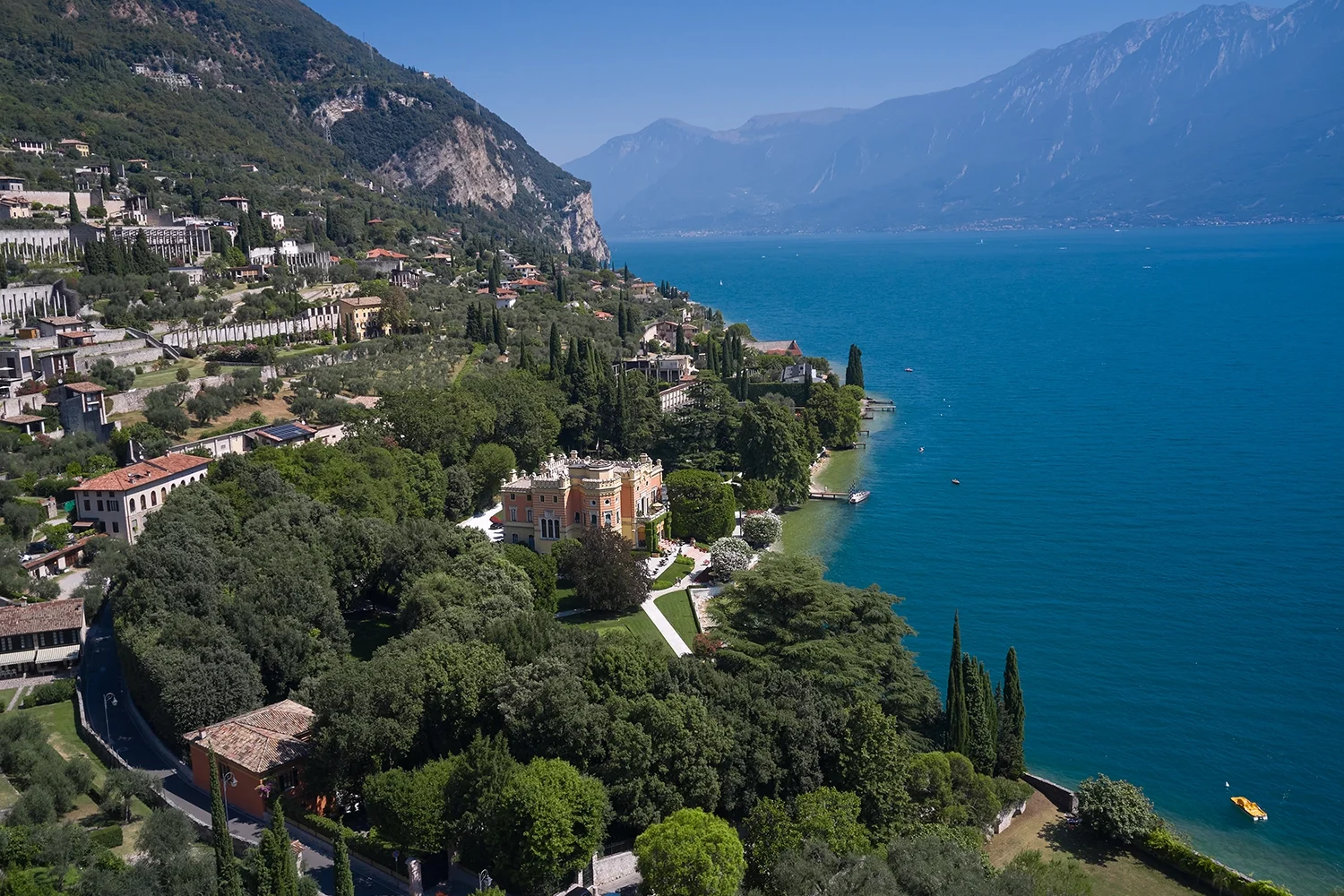 Lake Garda’s western shoreline with villas, cypress trees, and mountains dropping to vivid blue water.
