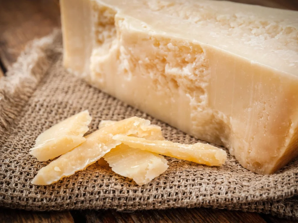Italy Moto Tours Close-up of a Parmigiano Reggiano cheese wedge with crunchy shavings on burlap over a wooden surface.