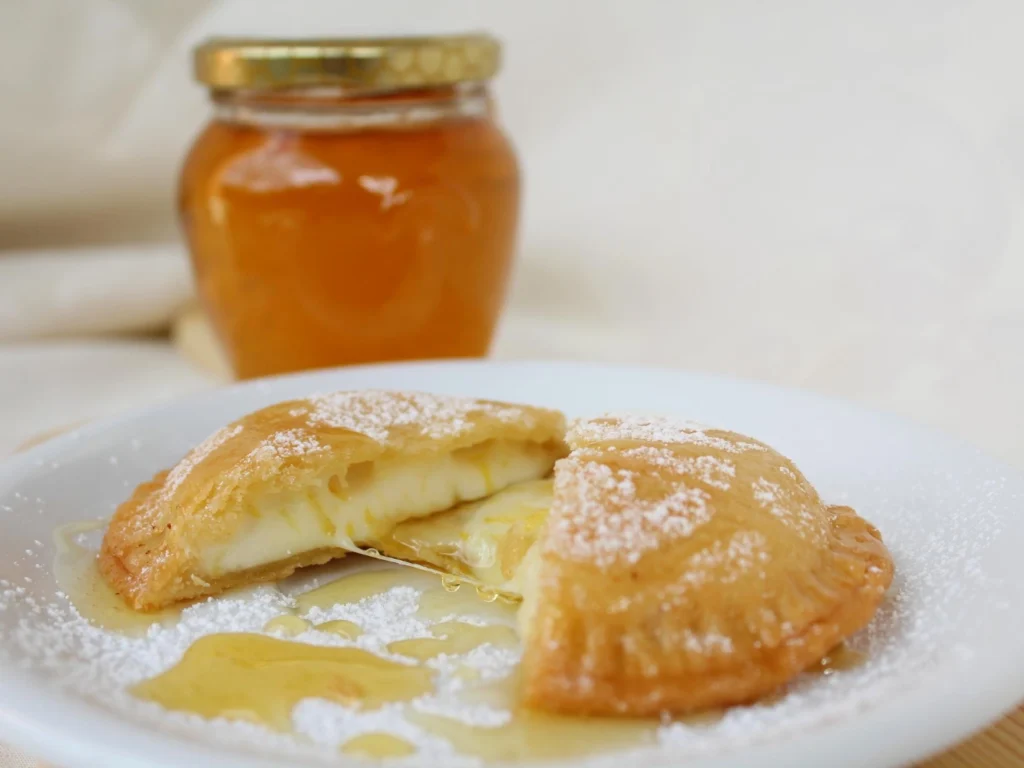 Italy Moto Tours Golden fried seadas filled with pecorino cheese and drizzled with honey on a white plate, jar of honey in background.