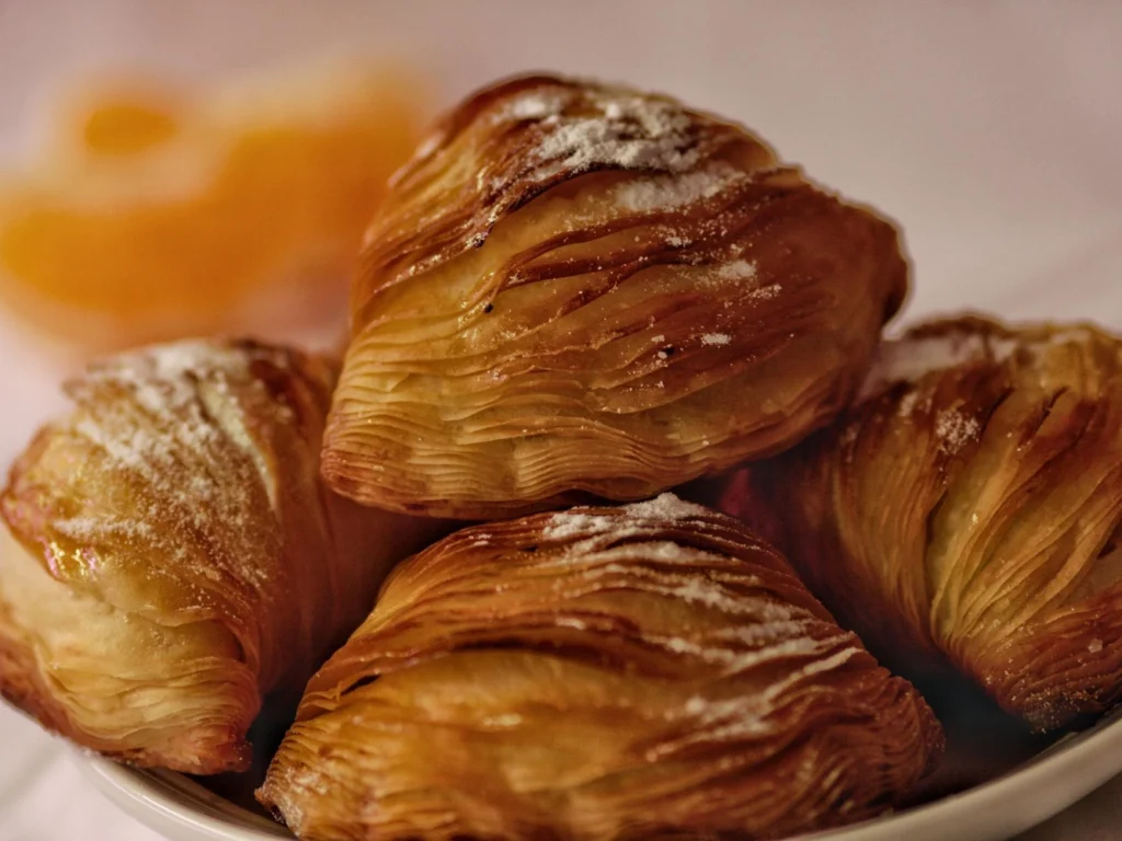 Italy Moto Tours Close-up of layered, shell-shaped sfogliatella pastries dusted with powdered sugar.