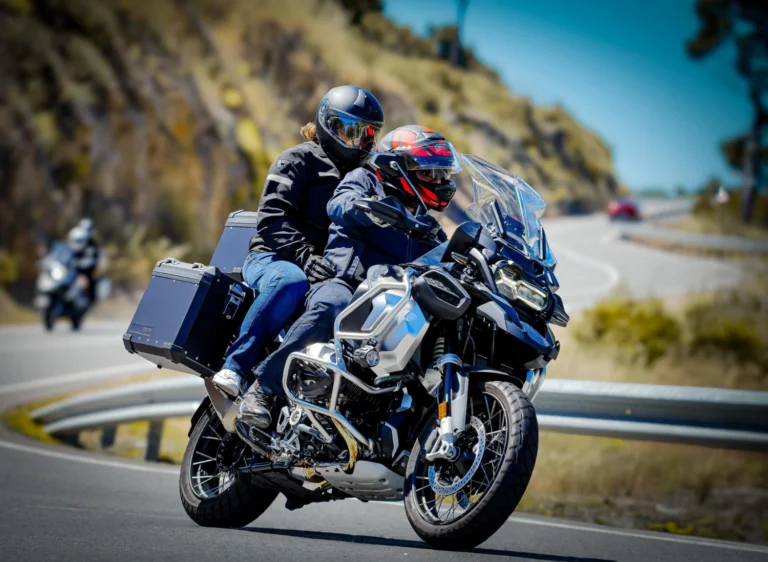 Italy Moto Tours Rider and passenger on a touring motorcycle leaning through a mountain hairpin with panniers on a sunny day.