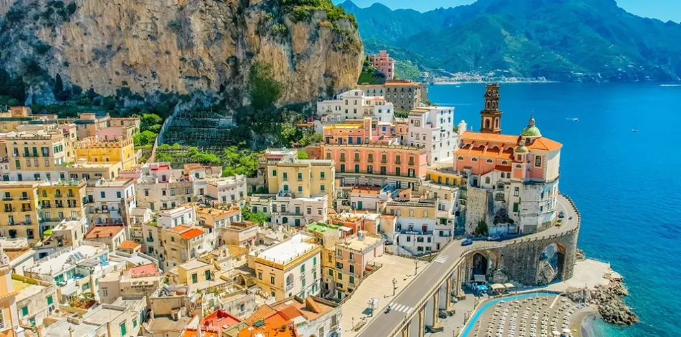 Aerial view of Atrani on the Amalfi Coast—pastel houses under cliffs, seaside church, and turquoise bay