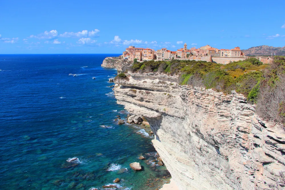 Italy Moto Tours Dramatic limestone cliffs with the clifftop town and citadel of Bonifacio, Corsica, above turquoise water