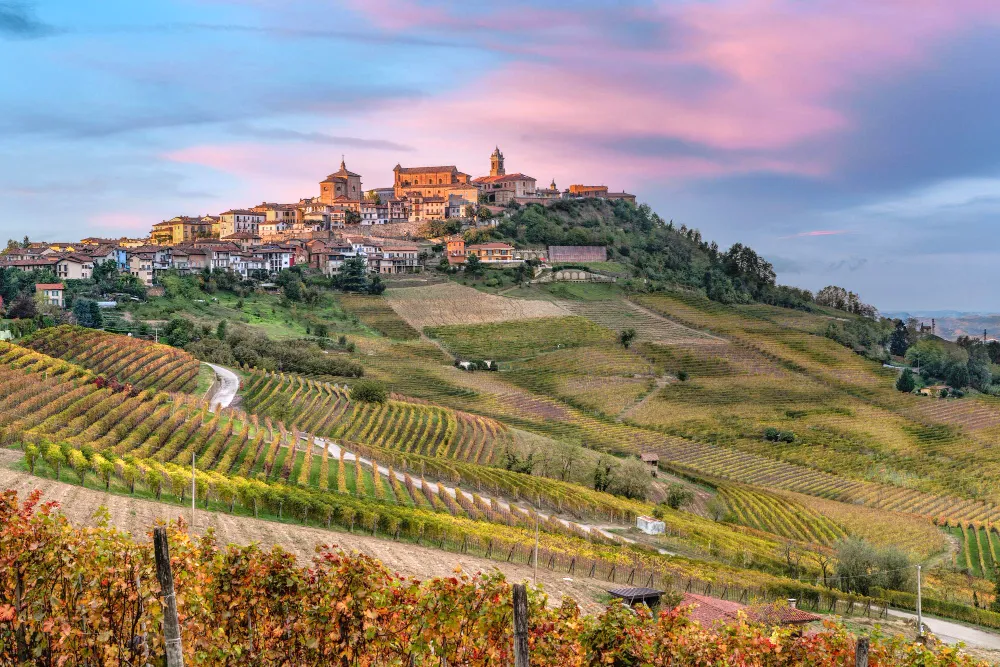 Italy Moto Tours Hilltop vineyards in the Chianti region of Tuscany, Italy, with rolling hills and a village at sunset.
