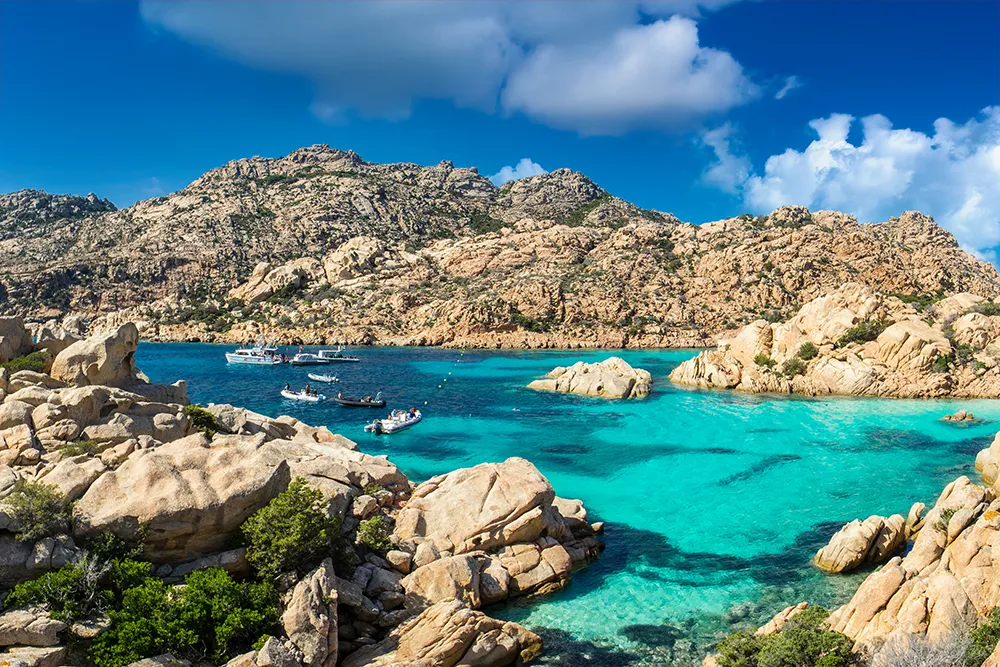 Italy Moto Tours Rocky coves and clear emerald water seen during a Costa Smeralda moto tour, with small boats anchored in a sheltered cove