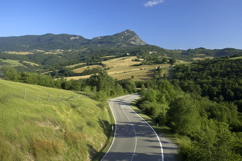 Italy Moto Tours Wide view of a winding asphalt road among forests and hills on Raticosa Pass