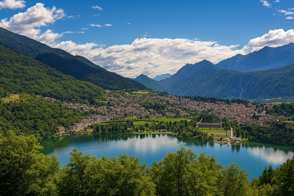Italy Moto Tours Panoramic view of Levico Terme on the shore of Lake Levico, surrounded by forested mountains in Trentino, Italy.
