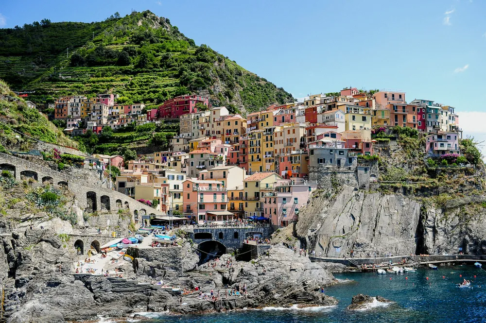 Italy Moto Tours Multicolored houses of Manarola clinging to the cliffs above the Ligurian Sea, with a small beach and boats below