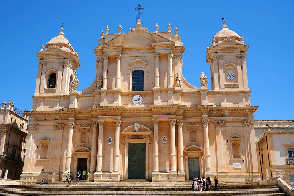 Italy Moto Tours Baroque Noto Cathedral in Noto, part of UNESCO Val di Noto — grand steps and twin towers under a clear sky.