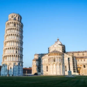 A wide view of the Leaning Tower of Pisa beside the cathedral in Piazza dei Miracoli on a clear blue-sky day.