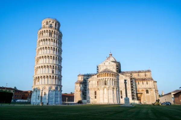 A wide view of the Leaning Tower of Pisa beside the cathedral in Piazza dei Miracoli on a clear blue-sky day.