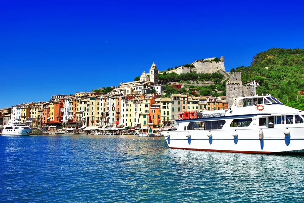 Italy Moto Tours Colorful Portovenere seafront with a white tour boat on bright blue water in Liguria, Italy