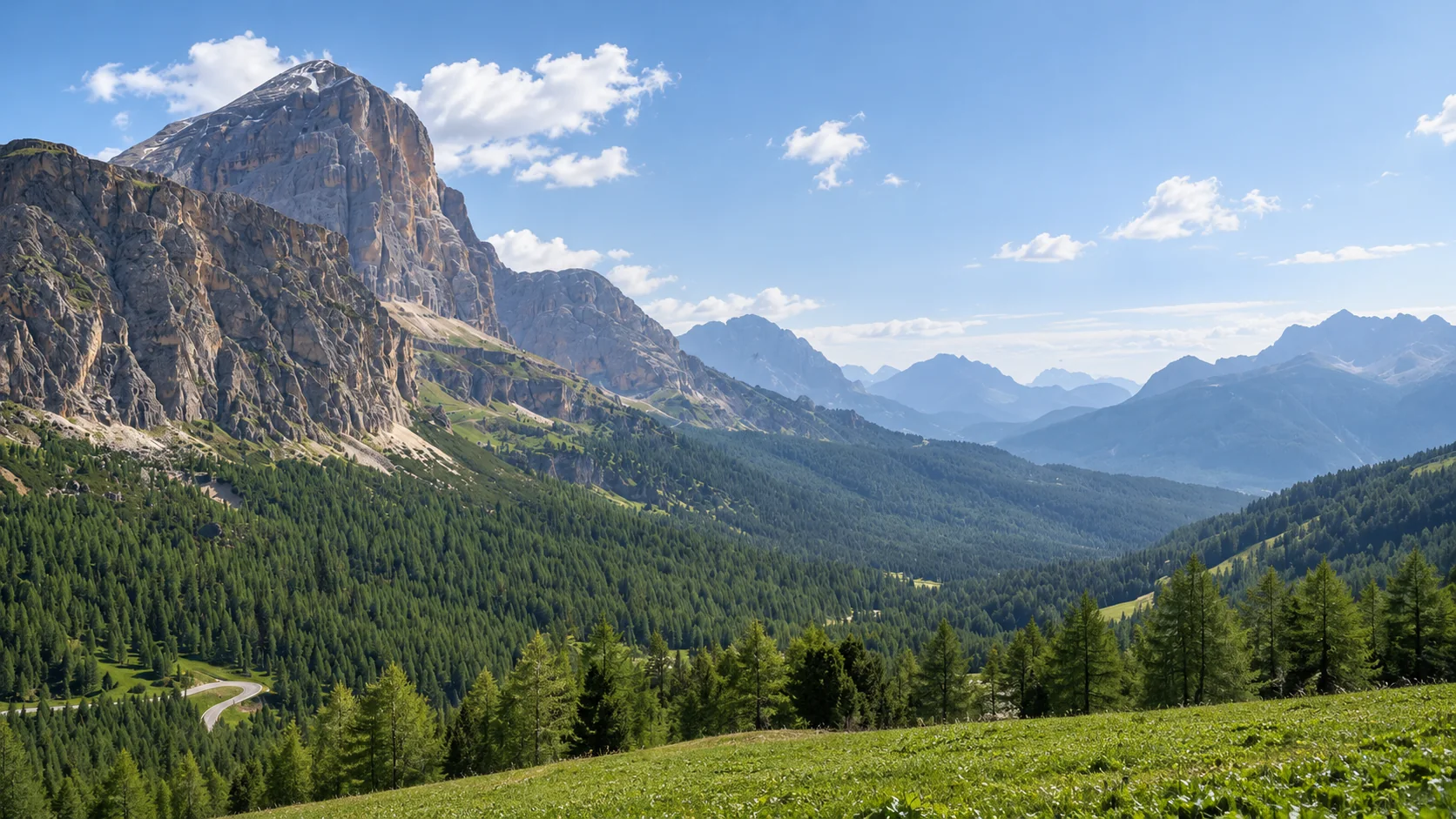 Pale Dolomite cliffs above a forested Alpine valley and a winding mountain road.