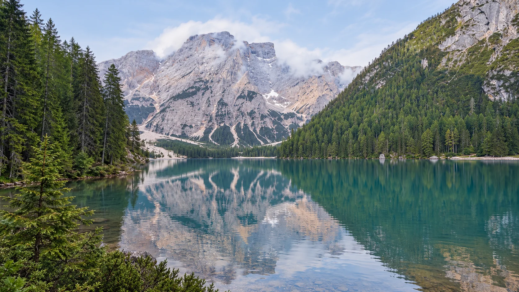 Alpine lake reflecting pale Dolomite mountains and forested slopes.