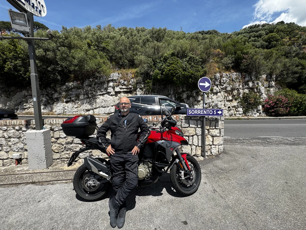 Motorcyclist beside a red touring motorcycle near a Sorrento road sign.