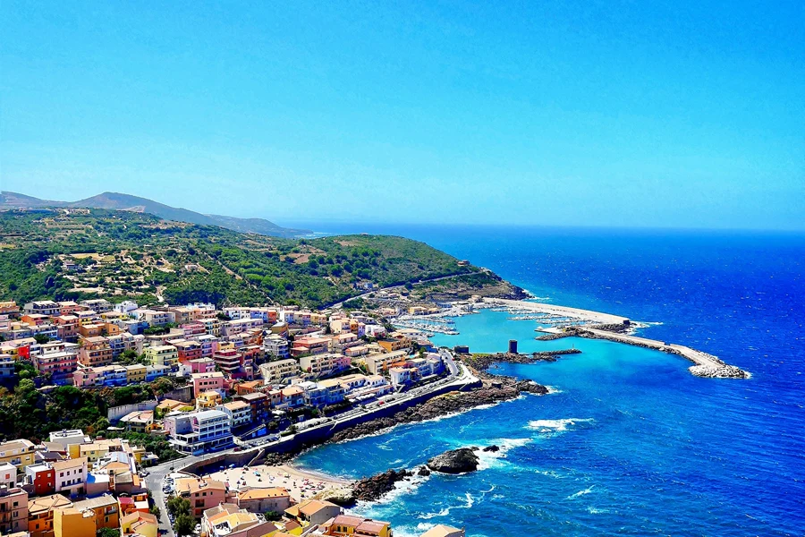 A colorful coastal town perched on cliffs above a turquoise Mediterranean harbor under a clear blue sky