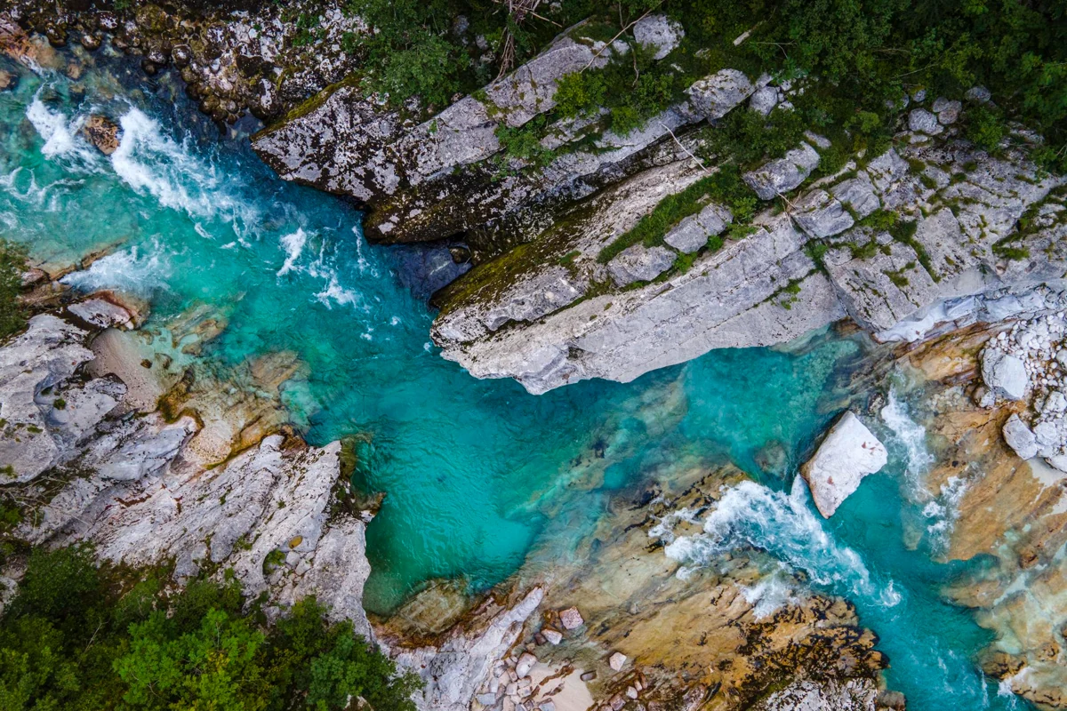 An overhead view of the turquoise Soča River flowing between rocky banks in Slovenia.