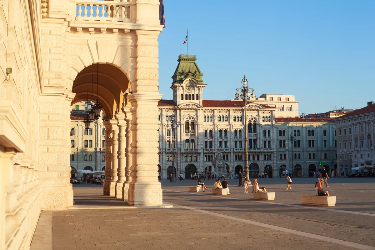 Sunlit arcades and historic buildings around Piazza Unità d’Italia in Trieste.